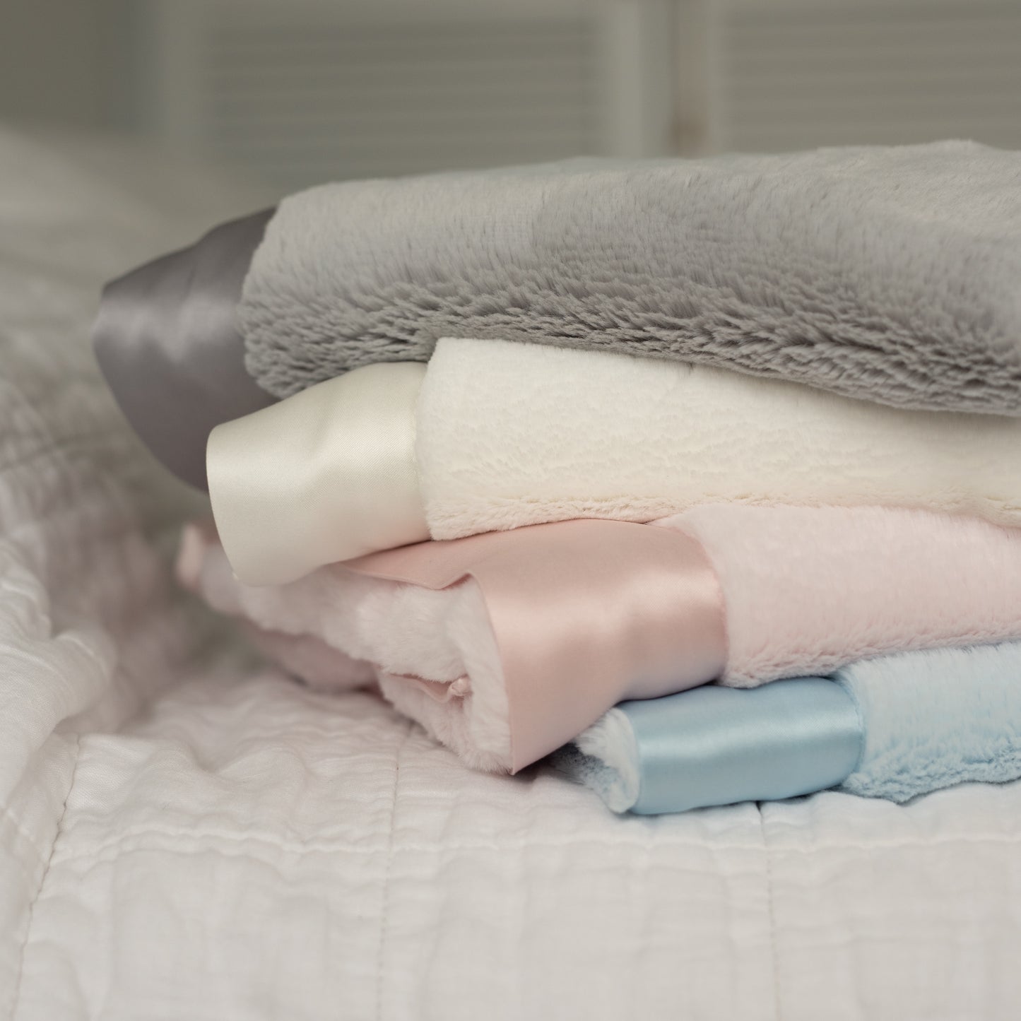 Close-up of four neatly folded luxury baby blankets, showcasing their ultra-soft texture and signature satin edges. Available in four elegant colours—blue, pink, grey, and white—these timeless keepsake blankets offer the perfect combination of comfort and style that lasts forever.