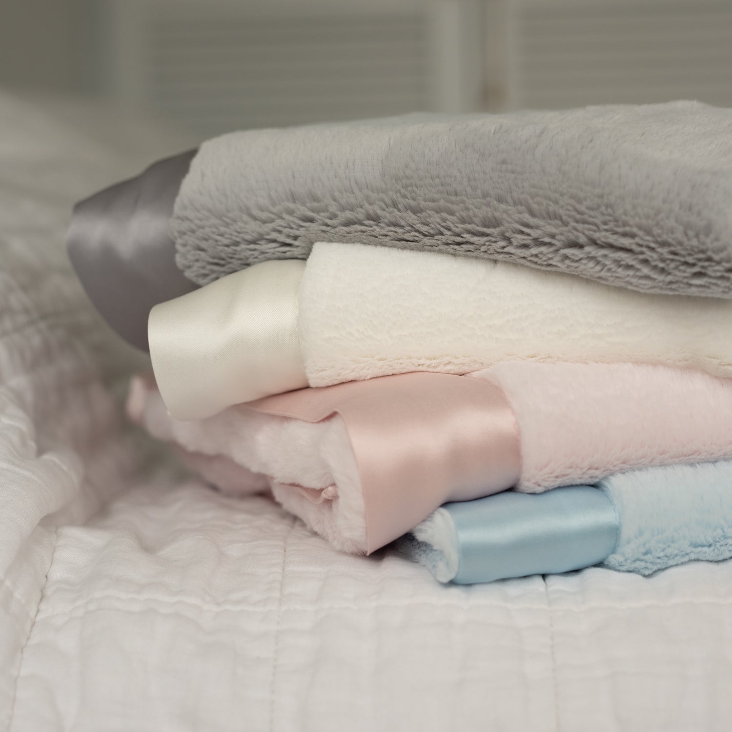 Close-up of four neatly folded luxury baby blankets, showcasing their ultra-soft texture and signature satin edges. Available in four elegant colours—blue, pink, grey, and white—these timeless keepsake blankets offer the perfect combination of comfort and style that lasts forever.