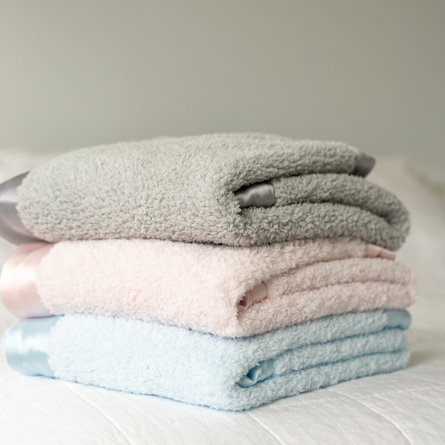 Three neatly folded Townhouse Blankets baby blankets in blue, pink, and grey chenille showing soft satin edge.