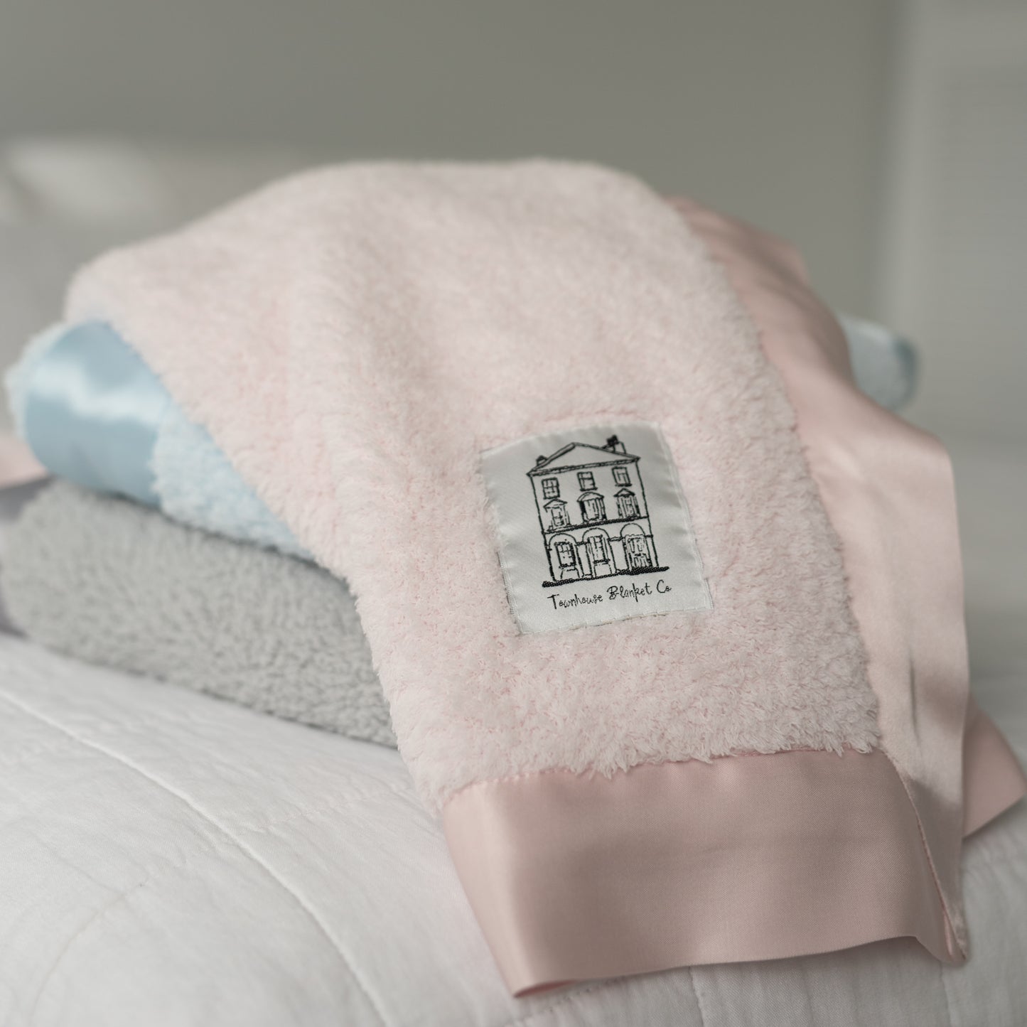 Three folded Townhouse Blankets baby blankets in grey, blue, and pink chenille with satin edges and logo patch showing colour range.