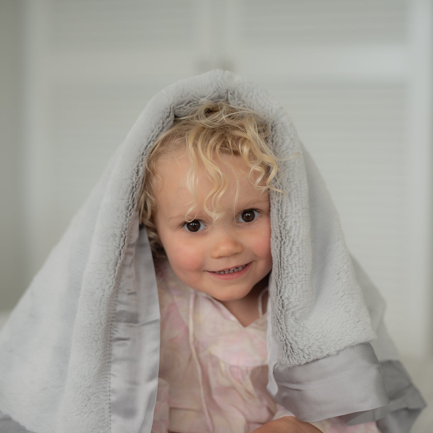 Blond child grinning with a grey Townhouse Blanket Company baby blanket over their head.