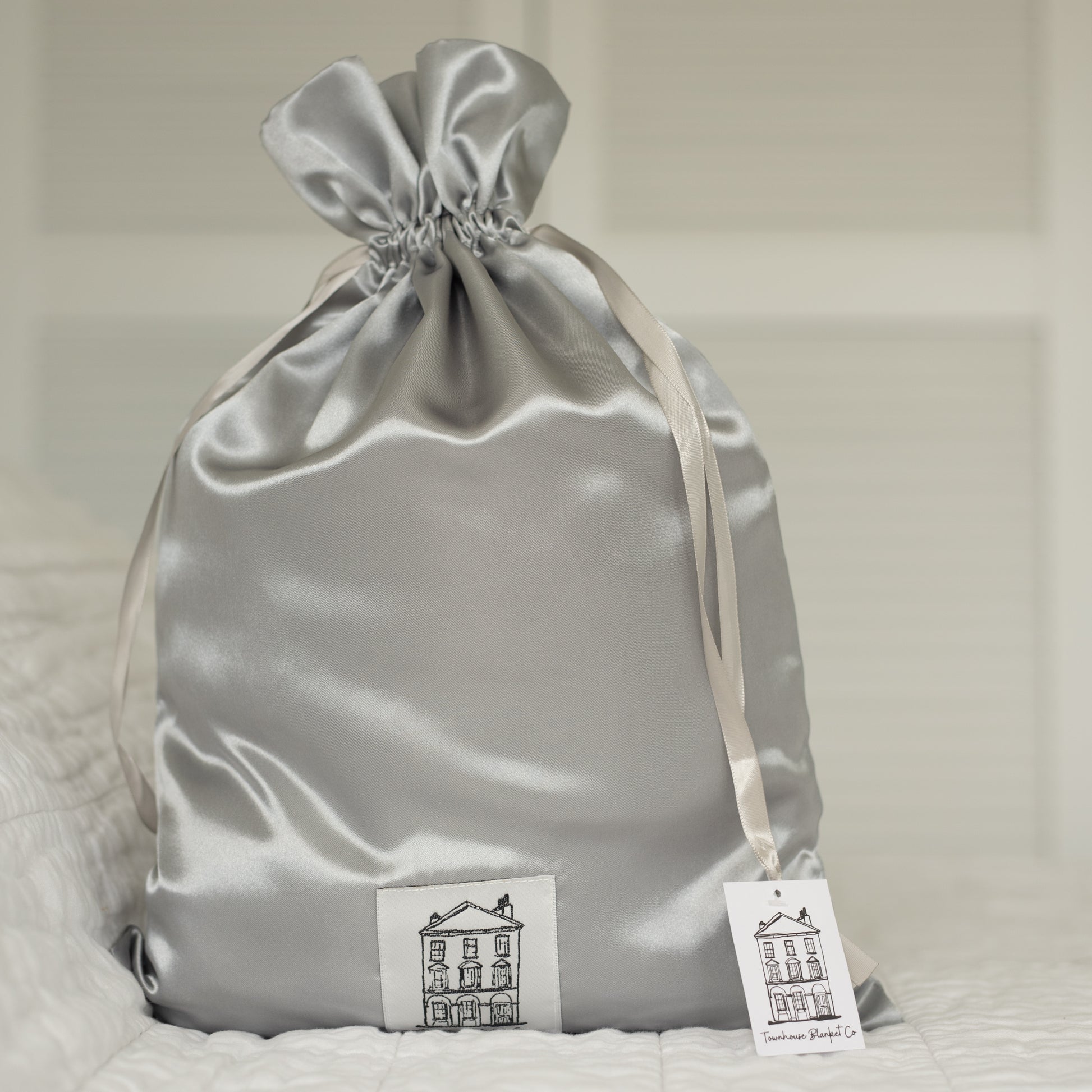 Exquisite grey satin drawstring gift bag, designed for timeless elegance. Features a signature Townhouse logo patch and a luxe gift tag for personalised messages—exclusively included with every Townhouse baby blanket for the ultimate gifting experience.